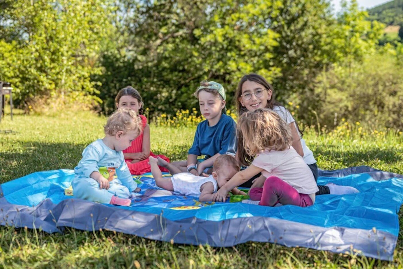 A group of children sitting on a blue blanket outdoors.