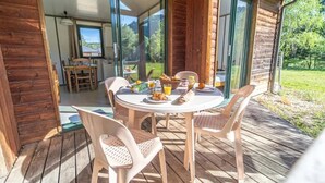 Terraza de madera con mesa y sillas redondas, desayuno incluido y vista a la vegetación.