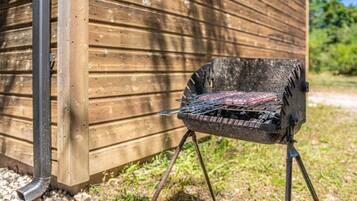 Un barbecue portable doté d’une grille en métal et fonctionnant au charbon de bois, placé sur un support à côté d’un bâtiment en bois.