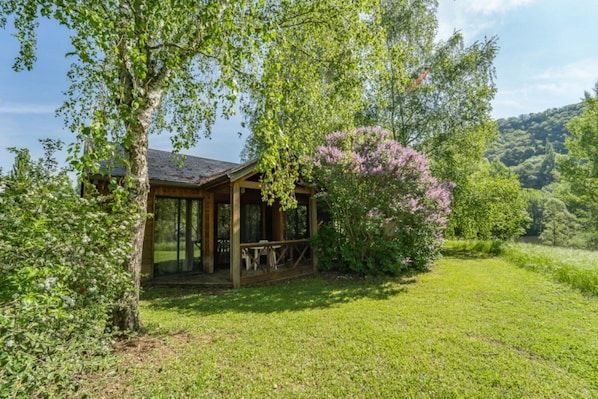 Une cabane en bois dotée d’un porche abrité, entourée d’une végétation luxuriante et d’arbustes en fleurs.