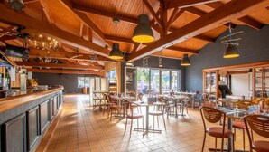 Een ruime eetzaal met houten balken, betegelde vloeren en meerdere tafels met stoelen.