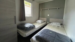 Een kleine, compacte kamer met twee eenpersoonsbedden, een raam met gordijnen, en een plank boven de bedden.