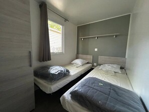 A small, compact room with two single beds, a window with curtains, and a shelf above the beds. - ZEcamping 4* familial piscine couverte chiens acceptés locatif TV 29m2 (Saint-Hilaire-de-Riez)