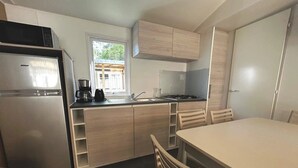 Eine kleine Küche mit Kühlschrank, Herd und Spüle. Ein Fenster sorgt für natürliches Licht und einen Ausblick.