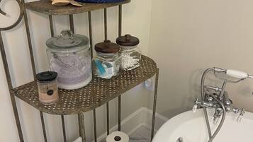 Un tocador de baño con un estante metálico que contiene artículos de aseo, una cesta azul y un lavabo blanco con grifo.