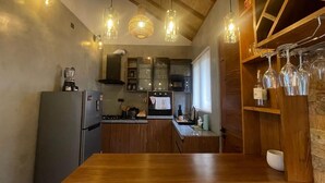 A kitchen with wooden cabinets, a granite countertop, a refrigerator, a stove, and hanging wine glasses. - Alo Kai Villa (Weligama)