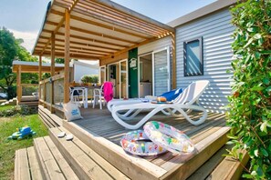 Eine überdachte Terrasse im Freien mit Liegestühlen und aufblasbaren Ringen, einem kleinen Tisch und einer Sitzgelegenheit mit Blick auf das Haus.