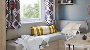 A cozy seating area with a cushioned bench, a striped pillow, and a white throw blanket. - ZEcamping 4* piscine couverte club enfant jacuzzi locatif TV LV clim (Aureilhan)