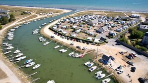An aerial view of a marina with boats docked along the water's edge, surrounded by residential buildings and a sandy beach. - ZEcamping 3* toboggans mobil-home TV 16m2 2 pers (Quinéville)