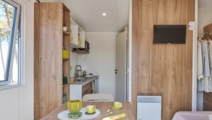 A compact room with a wooden wall, a bed with a pink blanket, a small kitchenette, and a window. - ZEcamping 3* toboggans mobil-home TV 16m2 2 pers (Quinéville)
