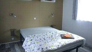 Een slaapkamer met een bed, twee wandplanken, een raam met gordijnen en een houten vloer.