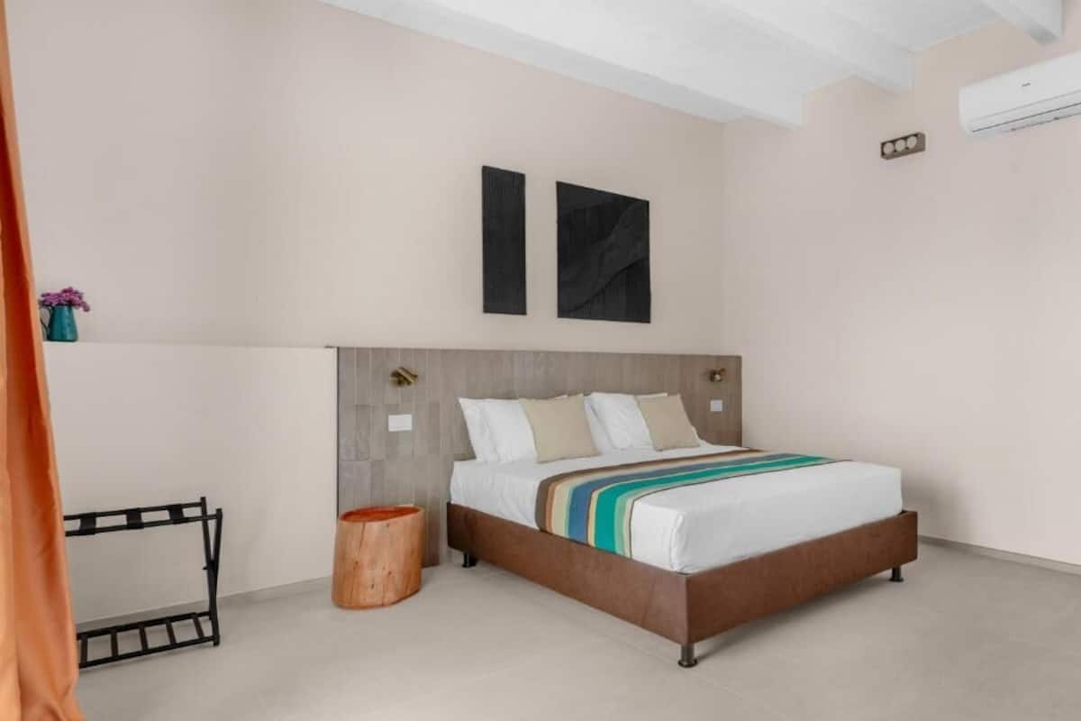 Un dormitorio moderno con cama, cabecera de madera, un taburete pequeño de madera y una estantería metálica negra.