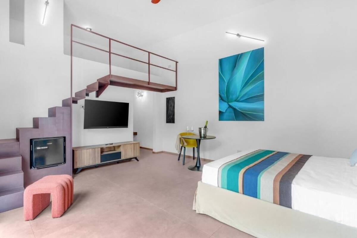 Un dormitorio moderno con una escalera, un televisor de pantalla plana, una cama con ropa de cama a rayas y un cuadro abstracto grande.