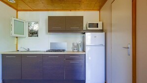 A compact kitchen with dark cabinets, a microwave, a refrigerator, and a window with a view of greenery.