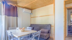 A cozy room with a wooden ceiling, a grey sofa, a dining table with chairs, and a window with curtains.