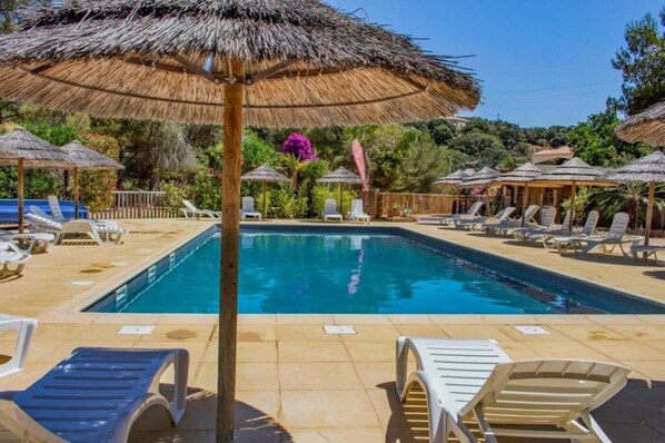 Una piscina con sillas de descanso y sombrillas de paja.