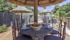 An outdoor dining area with wooden tables and chairs, thatched umbrellas, and a wooden deck.