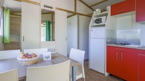 A compact kitchen with a red cabinet, a white refrigerator, and a microwave. There is a dining table with chairs and a basket of bread.