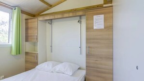 A bedroom with a bed, a wooden wardrobe, and a window with curtains.