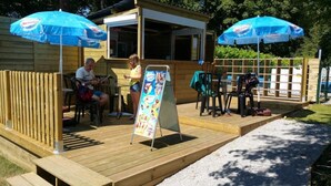 Eine Holzterrasse mit zwei blauen Sonnenschirmen, einer kleinen Holzhütte und einem Schild.