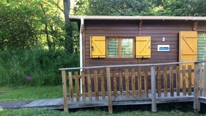 Une cabane en bois dotée d’une terrasse en bois et d’une rampe menant à une porte.
