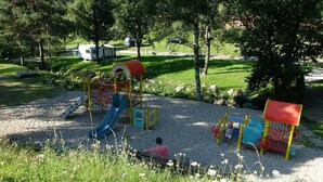 Une aire de jeux avec des toboggans et des structures d’escalade, entourée d’arbres et bordée d’une zone recouverte de gravier.