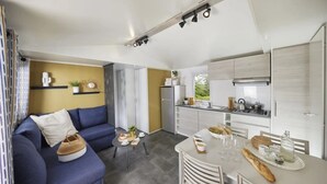 Un espacio habitable compacto con sofá, una mesa de comedor con pan y bebidas, y una kitchenette con estufa y refrigerador.
