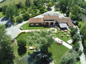 An aerial view of a building with a central courtyard, surrounded by trees and a small pond. - ZEcamping 3* animé piscine locatif TV clim 28m2 4 pers (Nailloux)