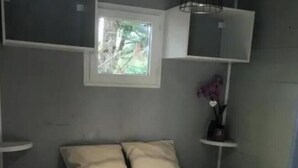 Une petite chambre à coucher, de taille réduite, comprenant un lit, deux oreillers, une fenêtre et une étagère sur laquelle est posé un vase.