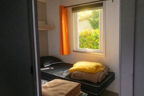 Ein kleiner, kompakter Raum mit Bett, einem Fenster mit Vorhängen und Blick ins Grüne.