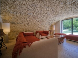 Un salon chaleureux avec un plafond en pierre, un canapé, une table basse et une vue sur la verdure à l’extérieur.