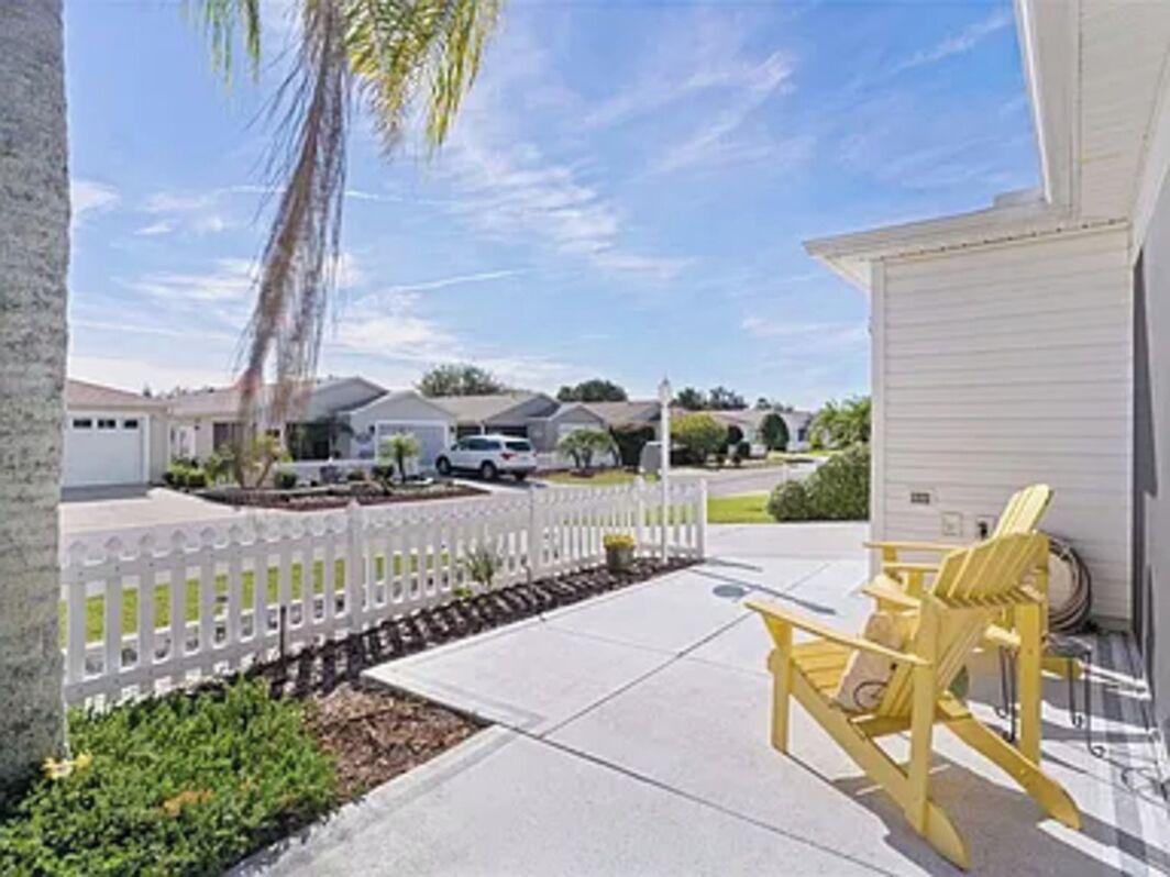 Un barrio residencial con cerca blanca de piquetes, una silla Adirondack amarilla y una puerta de garaje blanca.