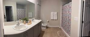 Ein Badezimmer mit zwei Waschbecken, einer Toilette, einer Dusche mit floralem Vorhang und einem Spiegel.