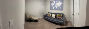 Ein Zimmer mit einer gebogenen dunkelblauen Couch, einem beigen Sessel, einem kleinen Tisch, einer Weltkarte an der Wand und einer weißen Tür.
