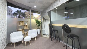 A reception area with a counter, white cushioned chairs, a wooden bookshelf, and a potted plant. - ROYAL İNN BORNOVA (İzmir)