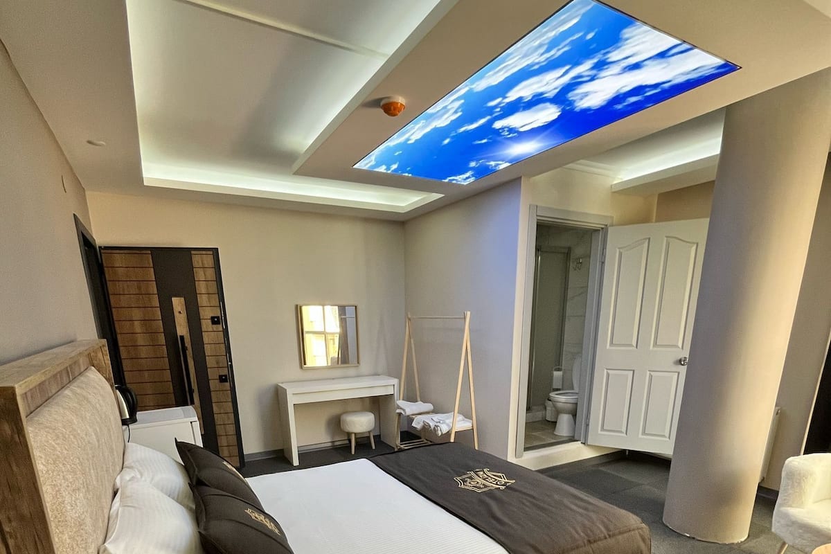 A modern hotel room with a large bed, a desk, a chair, and a ceiling skylight.