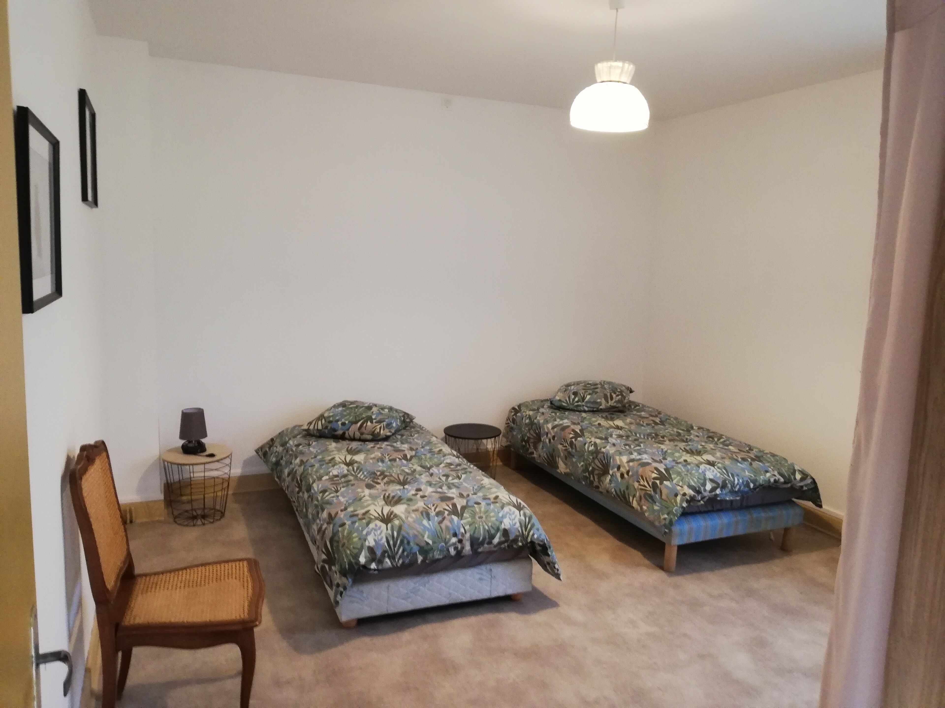 Un dormitorio con dos camas individuales, una silla, una mesita con una lámpara y un aplique.