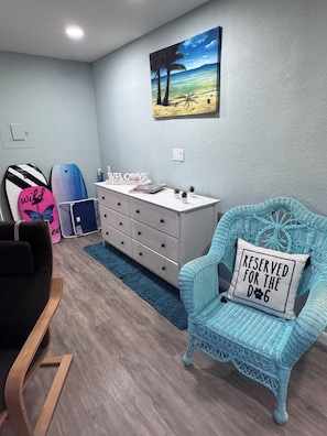 A room with a blue chair, a surfboard, and a wall-mounted painting. - Penguins on the Beach 2BR Beach & Pool  (Cocoa Beach)
