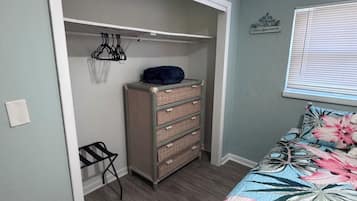 Ein Schlafzimmer mit Bett, Schrank mit Kleiderhaken und Fenster mit Jalousien.