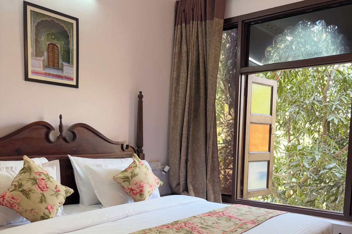 Una cama bien hecha con ropa de cama floral, cabecera de madera y ventana con vistas a zonas verdes.