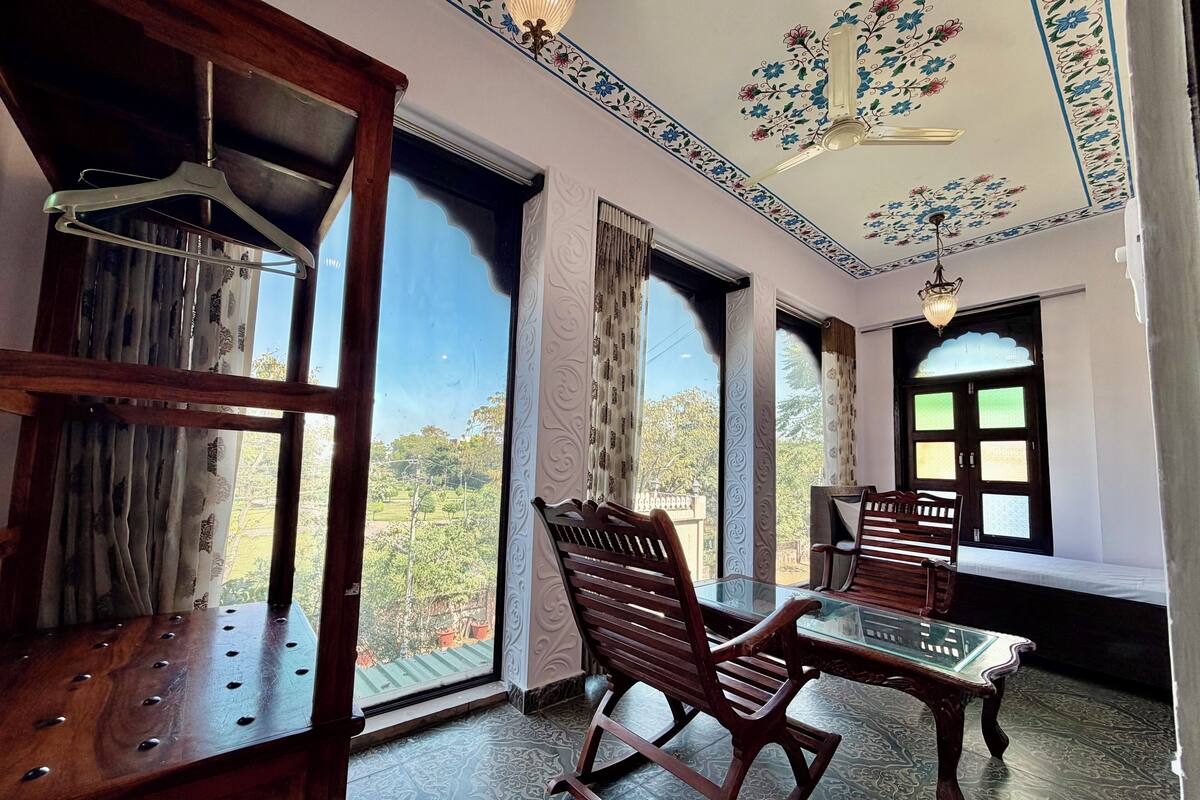 Una habitación con una silla de madera, una mesa de vidrio y vistas a la vegetación exterior.