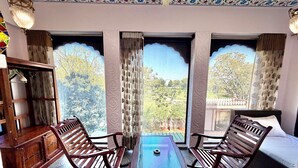 A room with two wooden chairs, a small table, a bed, and a cabinet. - Jharokha Heritage Hotel Jaipur (Jaipur)