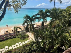 A beach view with a clear sky, palm trees, and a distant sailboat. - Coral Cove 8 Barbados Beachfront Apartment - Luxury, 3 bed, 3 bath, 2000 sq ft (Saint James)
