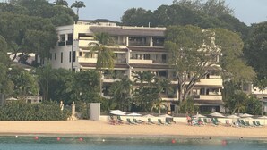 Un hôtel à plusieurs étages doté de balcons, avec une plage en premier plan et des palmiers.
