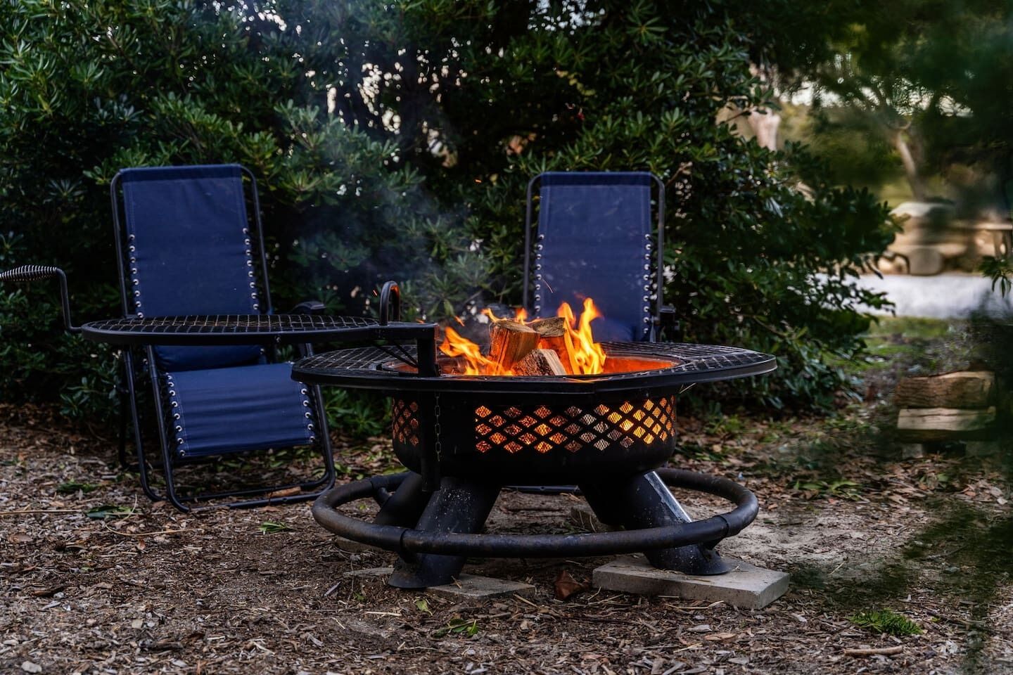 A fire pit with two chairs and a table in a garden setting.