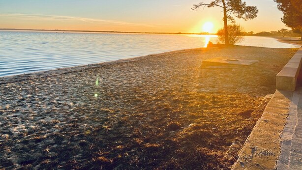 Een strand met een heldere lucht en de zon die in het water ondergaat.