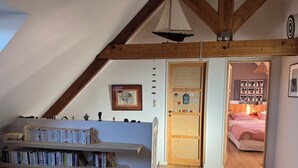 A cozy room with a sloped ceiling, wooden beams, a bookshelf, a bed with pink bedding, and a small sailboat decoration. - Family home in Belle-Ile-En-Mer (Le Palais)