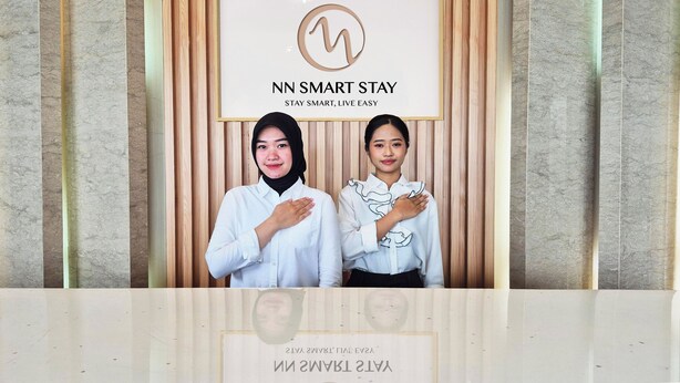 Deux personnes se tiennent devant une enseigne sur laquelle on peut lire : « NN SMART STAY » et « STAY SMART, LIVE EASY ».