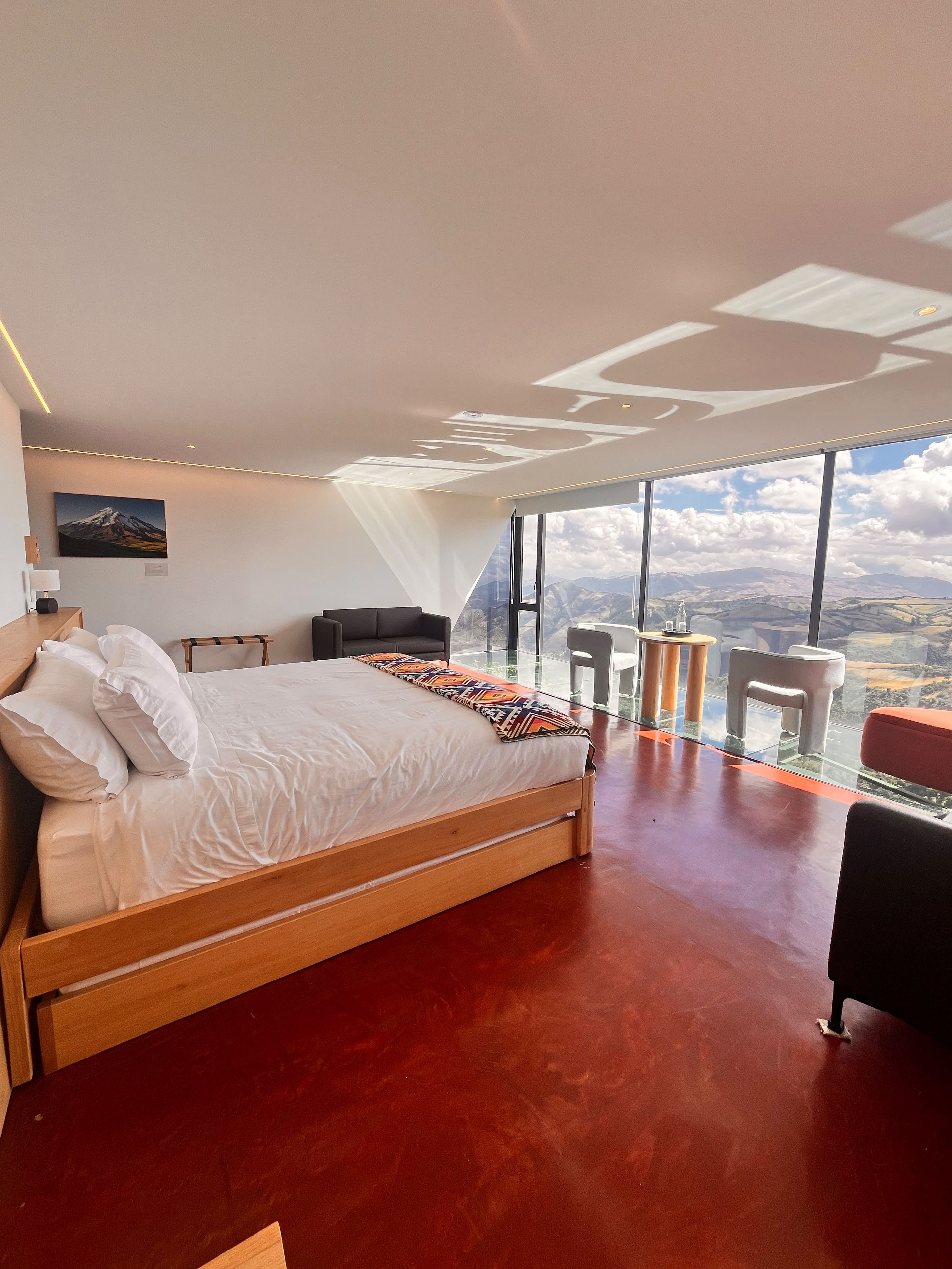Un dormitorio moderno con una cama grande, un escritorio y vistas a la montaña a través de amplios ventanales.