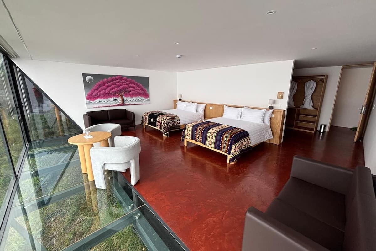 Una habitación de hotel moderna con piso de vidrio, dos camas, un sofá y una pequeña mesa.